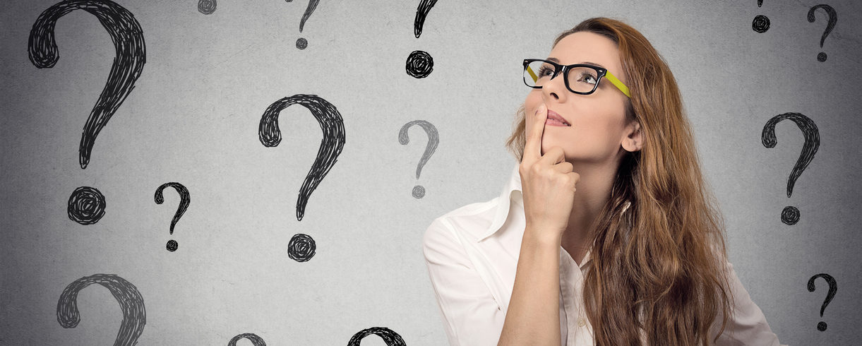 Business woman with glasses looking up at many question marks
